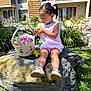 apartment_building, basket, bunny, child, curly_hair, easter_egg, flower, grass, greenery, hair_tie, outdoor, pink_dress, plant, rock, shoe, spring, sunlight, toddler, white_shoe, window