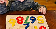 Archer is registered to the contest to win money with this photo: child, toddler, puzzle, wooden_puzzle, numbers, colorful, table, indoor, smiling, happy, playing, toy, learning, education, furniture, clothing, person, young_child, wood, casual
