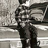 child, boy, plaid_shirt, jeans, boots, vintage_truck, outdoor, black_and_white, nature, trees, rustic, portrait, side_view, casual_clothing, weathered, old_vehicle, sitting, young, nostalgic, monochrome