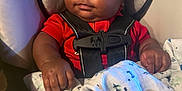 Delijah is registered to the contest to win money with this photo: baby, infant, car_seat, blanket, red_clothing, child, seat_belt, curly_hair, indoors, cute, chubby_cheeks, holding, fabric, patterned_blanket, safety, portrait, young_child, closeup, infant_baby, baby_hands