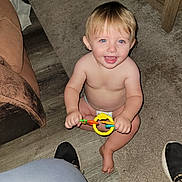 Ayden is registered to the contest to win money with this photo: toddler, child, smiling, toy, indoor, carpet, floor, barefoot, diaper, blue_eyes, blond_hair, furniture, living_room, person, happy, sitting, cute, playful, young_child, home