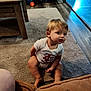 Ayden is registered to the contest to win money with this photo: toddler, child, carpet, living_room, onesie, wooden_table, playpen, floor, person, furniture, baby, indoors, pet_bowls, curious, seated, expression, home, light, face, legs