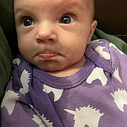 Maylee is registered to the contest to win money with this photo: baby, infant, face, purple_clothing, unicorn_pattern, curious_expression, close_up, person, child, cute, apparel, portrait, sitting, indoors, young_child, head, eyes, skin, mouth, baby_garment