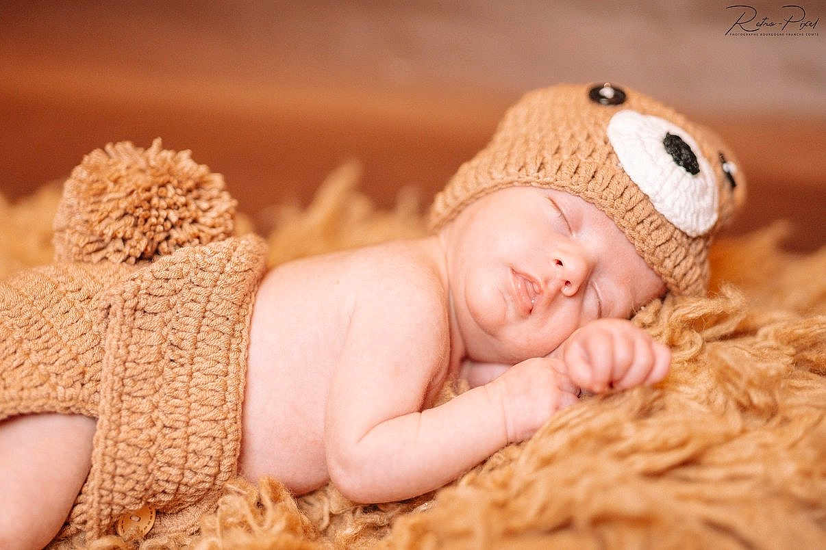 Ilyano a rejoint le concours — aidez-le/la à gagner de superbes lots ! baby, newborn, sleeping, knit_hat, pompom, blanket, fur_blanket, cozy, infant, portrait, soft_lighting, cute, peaceful, hand, face, closed_eyes, skin, studio_photo, warm_tones, props