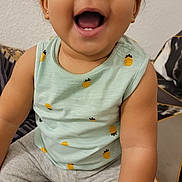 Léa a rejoint le concours — aidez-le/la à gagner de superbes lots ! baby, child, smiling, happy, cute, curly_hair, pineapple_pattern, sleeveless_shirt, pants, sitting, indoor, cushion, geometric_pattern, hand, portrait, face, skin, eyes, mouth, joy