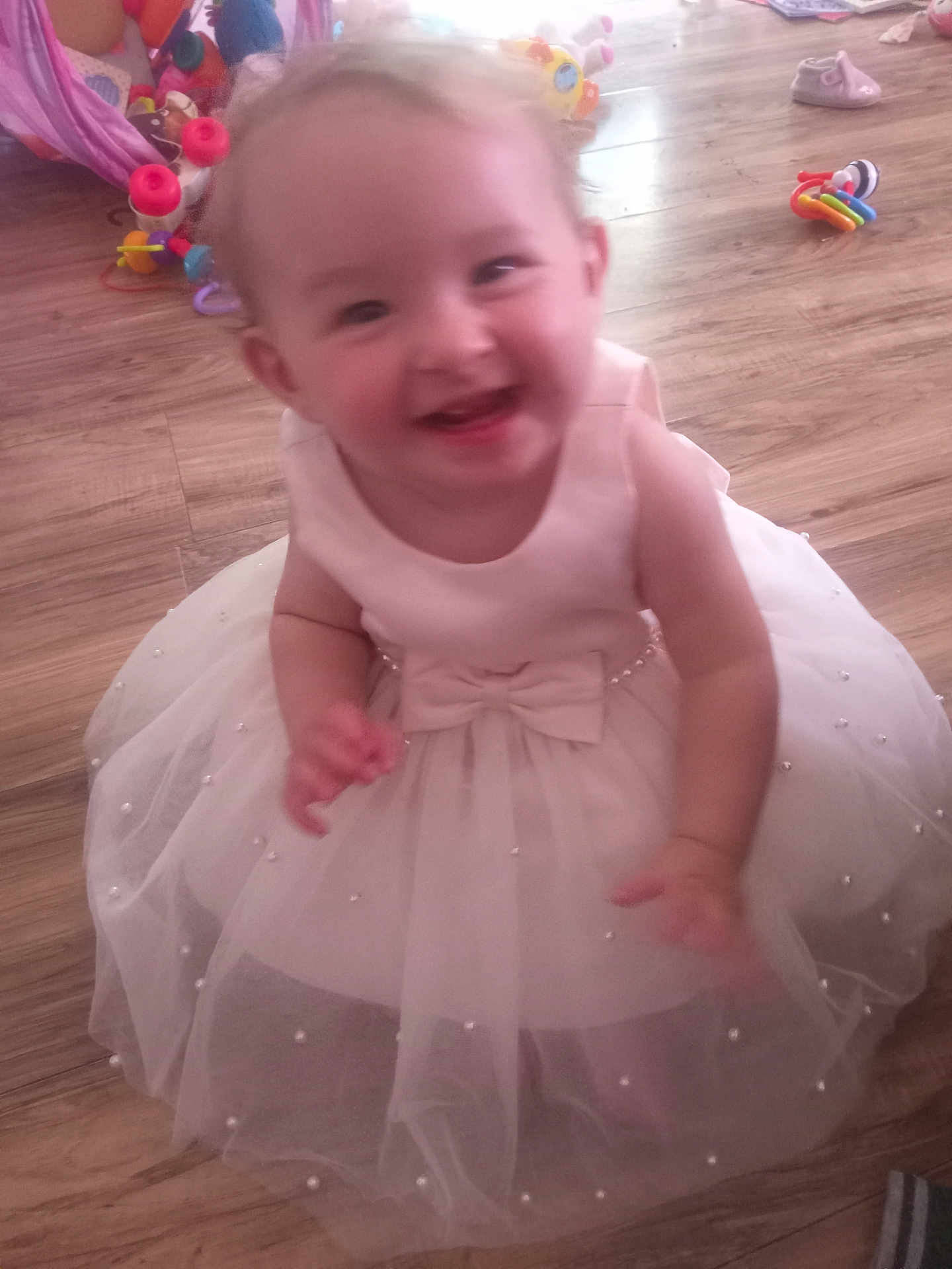 Addison joined the competition — help win amazing prizes! toddler, child, dress, white_dress, pearl_embellishments, smiling, happy, indoor, wooden_floor, toys, colorful_toys, baby, person, cute, motion_blur, floor, playtime, girl, infant, celebration