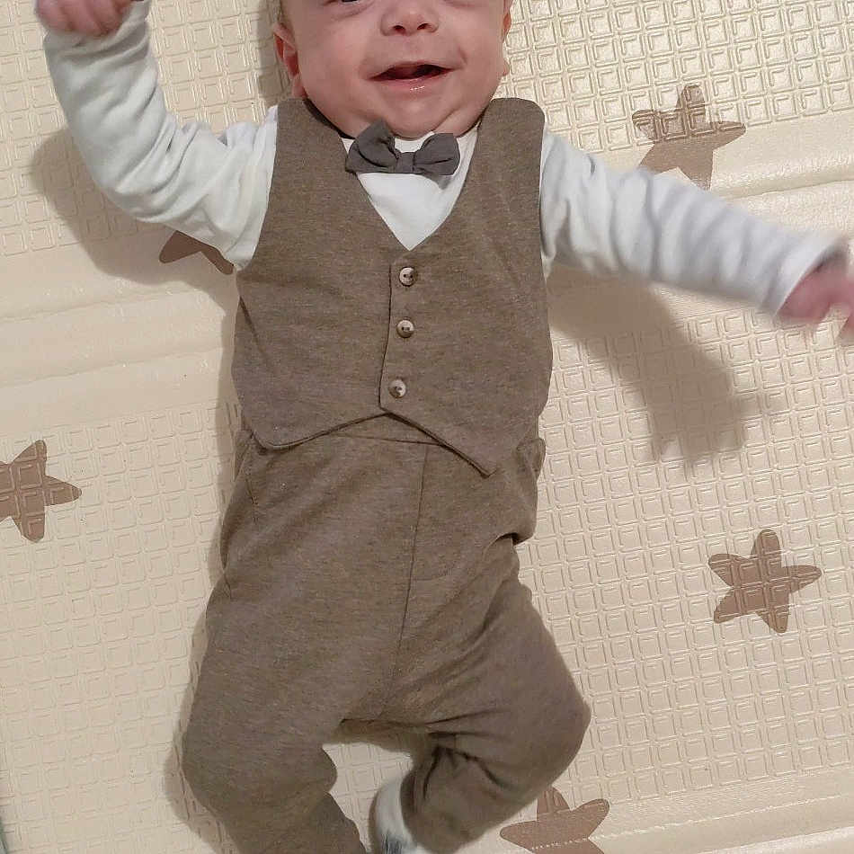 Elyjah a rejoint le concours — aidez-le/la à gagner de superbes lots ! baby, bow_tie, child, clothing, cute, funny_pose, happy, indoors, infant, lying_down, mat, person, portrait, raised_arm, small, smiling, soft_lighting, star_pattern, vest, white_socks