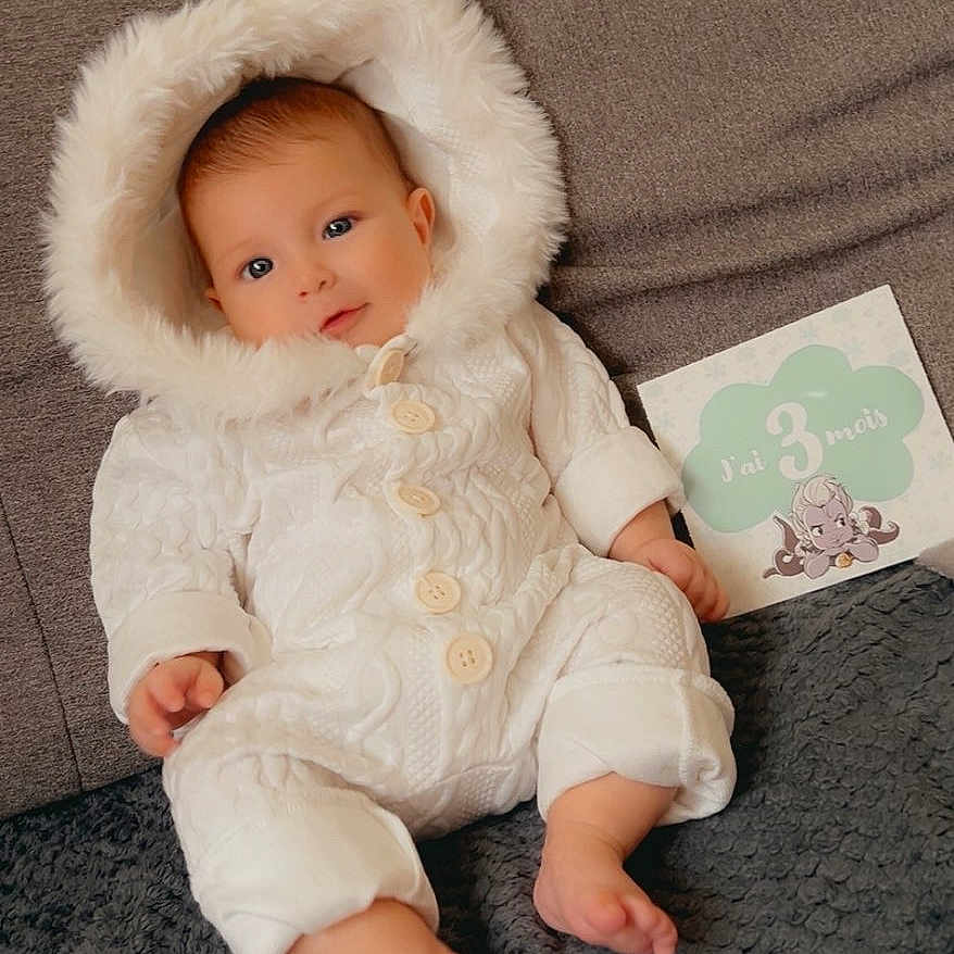 Amaya participe au concours pour gagner de l'argent avec cette photo : 3_months, baby, blanket, child, couch, cozy, cute, face, happy, hood, indoors, infant, milestone_card, person, portrait, sitting, smiling, soft_texture, warm_clothing, white_onesie