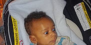 Ezekiel joined the competition — help win amazing prizes! baby, infant, car_seat, blanket, clothing, onesie, face, person, indoor, kitchen, refrigerator, cabinet, curly_hair, child, seated, looking_away, warning_label, soft_toy, home, curious