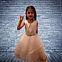 child, girl, dress, pink, waving, brick_wall, wooden_floor, indoor, portrait, smiling, formal_wear, young, cute, fashion, posing, person, background, floor, wall, standing