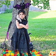 Abbigail is registered to the contest to win money with this photo: child, girl, black_dress, tree, halloween, bat_decoration, hand_decoration, pumpkin, blanket, grass, outdoor, costume, braids, decorations, spooky, fall, holiday, yard, fence, boots