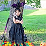child, girl, black_dress, tree, halloween, bat_decoration, hand_decoration, pumpkin, blanket, grass, outdoor, costume, braids, decorations, spooky, fall, holiday, yard, fence, boots