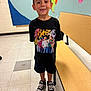 Antonio is registered to the contest to win money with this photo: bench, boy, casual_clothing, child, classroom, converse_shoes, floor, graphic_tshirt, hair, happy, indoor, map, person, portrait, school, shorts, smiling, standing, tiled_floor, wall