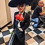 black_jacket, black_skirt, chair, checkered_floor, child, earrings, floor_tiles, glasses, indoor, man, mariachi, musical_instrument_case, person, red_bow, seated, smiling, sombrero, table, traditional_clothing, white_shirt