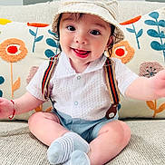Theo is registered to the contest to win money with this photo: baby, child, smiling, hat, striped, bunny_ears, suspenders, white_shirt, blue_shorts, socks, couch, cushions, floral_pattern, indoor, cute, happy, portrait, sitting, toddler, cozy