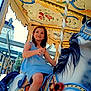 amusement_park, blue_dress, carousel, child, colorful, daylight, decorative, entertainment, festival, fun, girl, happy, horse, joy, motion, outdoor, playful, ride, smiling, summer