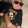 baby, sunglasses, nike, onesie, hand, couch, indoor, person, child, fingernail, casual, relaxed, furniture, home, infant, clothing, sitting, skin, adult, accessory