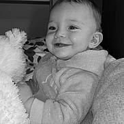 Youri a rejoint le concours — aidez-le/la à gagner de superbes lots ! baby, smiling, teddy_bear, cozy_clothing, indoor, black_and_white, child, cute, portrait, happy, soft_texture, plush_toy, infant, face, person, closeup, warm, joyful, holding, emojis