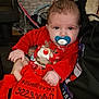 adult, baby, blue_eyes, brick_wall, child, cozy, cute, dress, face, festive, furniture, hand, holding, holiday_outfit, indoor, pacifier, person, red_clothing, reindeer, sitting