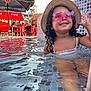 child, girl, pool, water, hat, sunglasses, pink_sunglasses, curly_hair, smile, swimsuit, tiled_pool, sunlight, outdoor, red_chairs, umbrella, coca_cola, schweppes, happy, summer, splashing