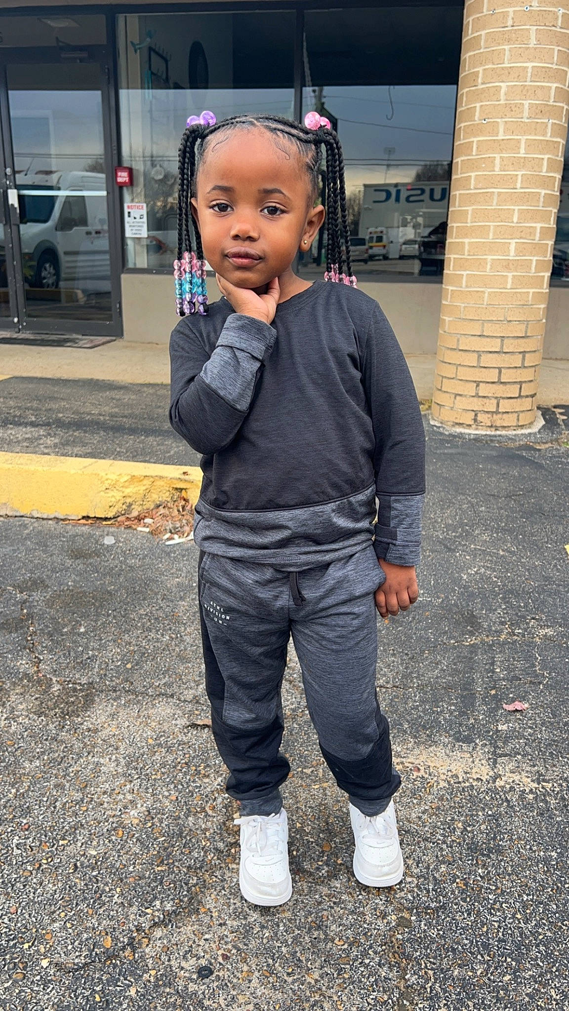 Nia is registered to the contest to win money with this photo: asphalt, audio_equipment, child, denim, eye, eyewear, face, formal_wear, hair, person, road_surface, sidewalk, sleeve, standing, street, t_shirt, tire, toddler, waist, walking