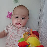 Meryl participe au concours pour gagner de l'argent avec cette photo : baby, baby_girl, child, childcare, clothing, colorful, crib, cute, face, happy, indoor, infant, lying_down, pacifier, pink, plush_toy, smile, soft, toy, white