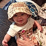 De'Shawn joined the competition — help win amazing prizes! baby, child, hat, bucket_hat, smiling, indoor, person, pillow, blanket, hand, plaid, clothing, cute, sitting, young_child, cozy, patterned, happy, supporting_hand, casual