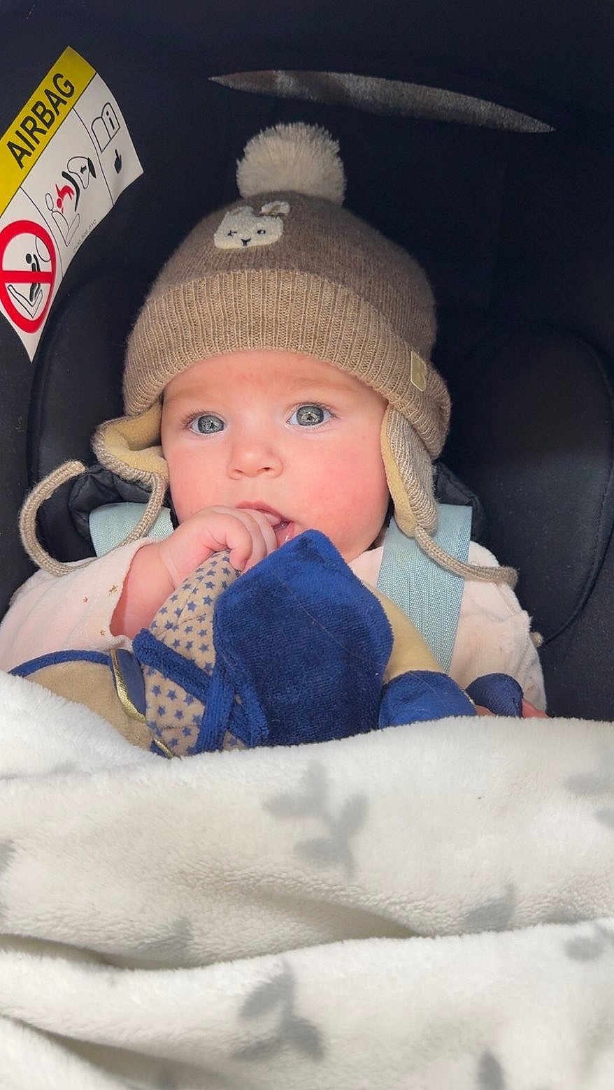 Romy participe au concours pour gagner de l'argent avec cette photo : baby, child, hat, knitted_hat, pom_pom, blanket, car_seat, blue_eyes, toy, cute, infant, warm_clothing, indoor, closeup, face, person, winter_wear, soft_toys, sitting, bundle