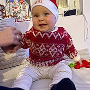 Hadriel participe au concours pour gagner de l'argent avec cette photo : adult, baby, black_socks, child, christmas, cozy, cute, decor, festive, hand, happy, holiday, indoor, red_sweater, santa_hat, seated, smiling, toy, white_pants, window