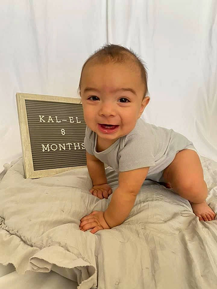Kal-el is registered to the contest to win money with this photo: baby, baby_toddler_clothing, cheek, child, comfort, facial_expression, finger, flash_photography, flooring, hairstyle, happy, linens, mammal, person, product, skin, sleeve, smile, standing, t_shirt
