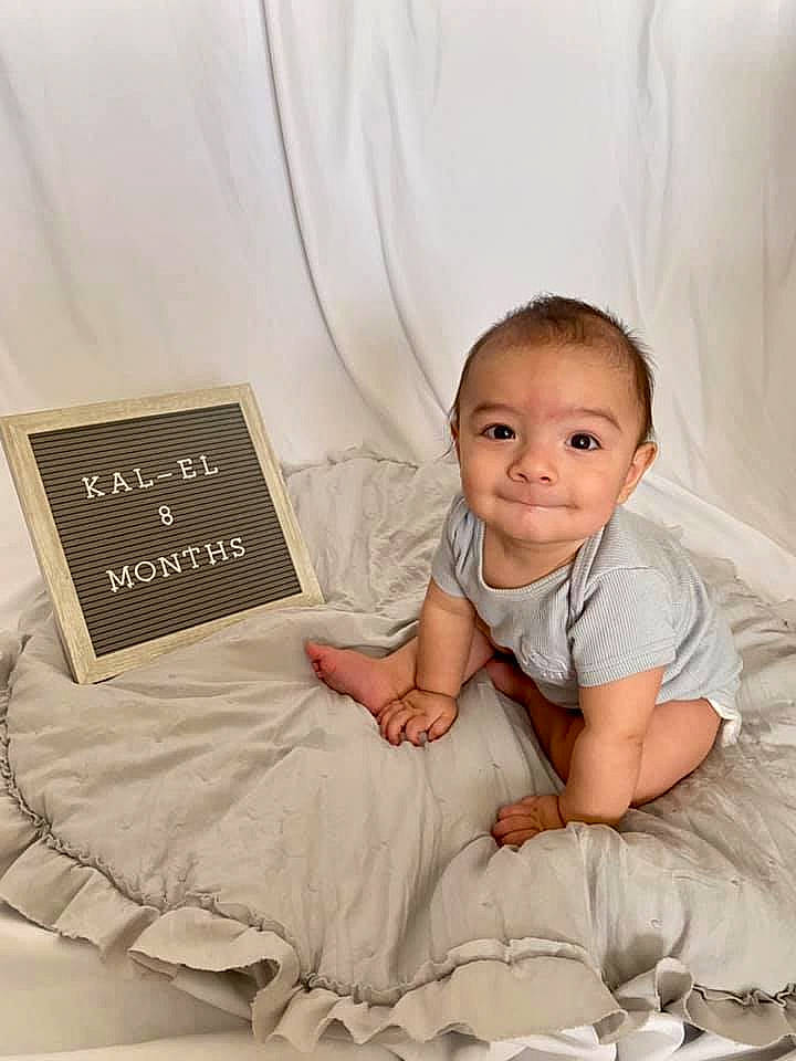 Kal-el is registered to the contest to win money with this photo: baby, baby_toddler_clothing, barefoot, bedding, book, child, comfort, flash_photography, flooring, happy, joy, linens, pattern, person, room, sitting, sleeve, smile, t_shirt, throw_pillow