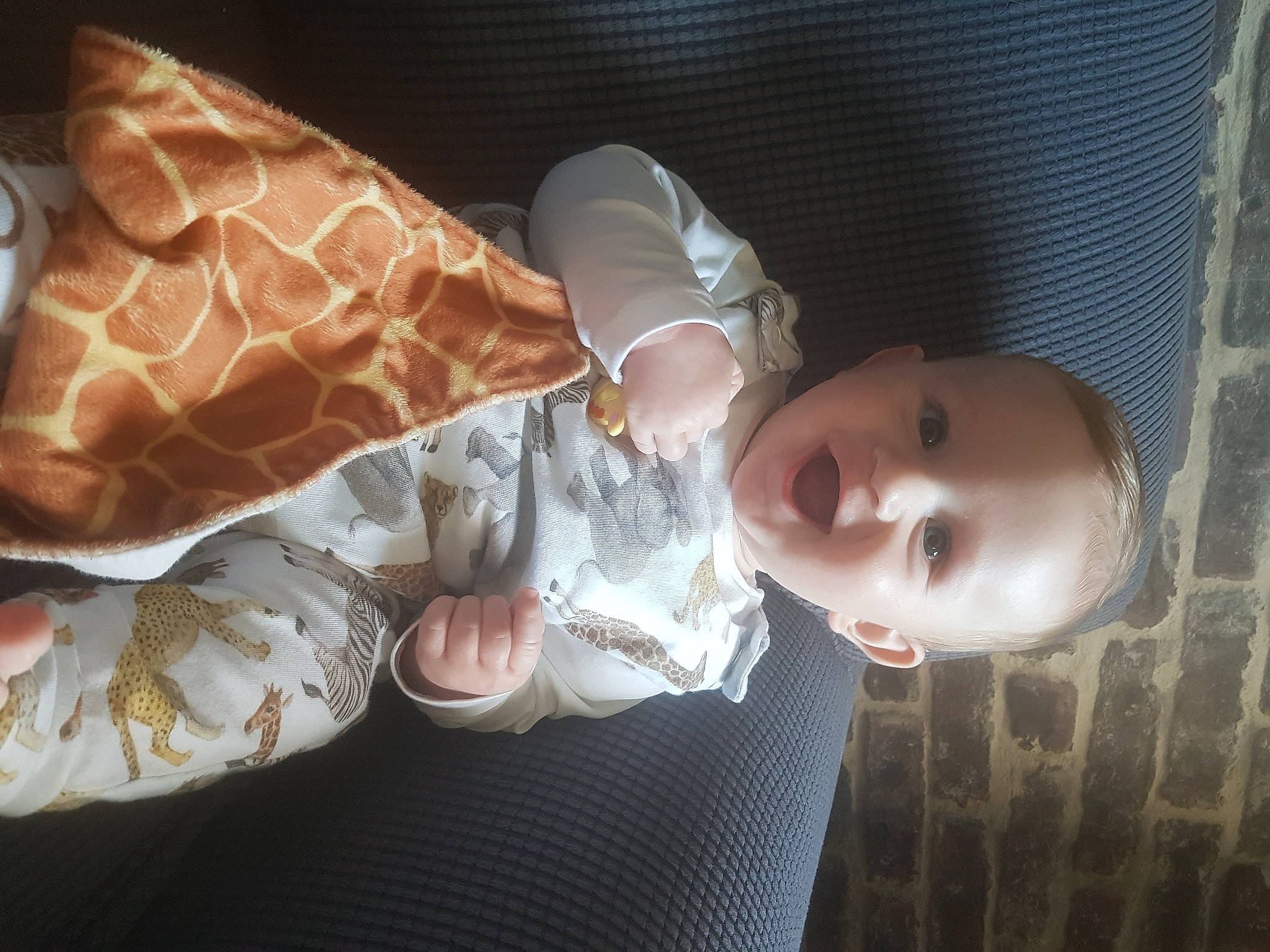 Chester is registered to the contest to win money with this photo: baby, baby_toddler_clothing, child, comfort, fashion_accessory, finger, human_leg, linens, mammal, pattern, person, room, smile, textile, toddler, vertebrate