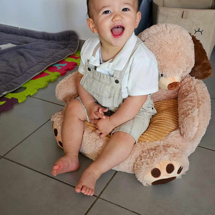 Aaron a rejoint le concours — aidez-le/la à gagner de superbes lots ! baby, barefoot, child, cute, floor_tiles, furniture, happy, home, indoor, overalls, person, play_mat, plush_toy, portrait, sitting, smiling, teddy_bear, toddler, toys, white_shirt