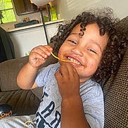 Cameron is registered to the contest to win money with this photo: casual, child, clothing, couch, curly_hair, face, food, hair, happy, home, indoor, meal, messy, person, playful, relaxed, sauce, smiling, spaghetti, toddler