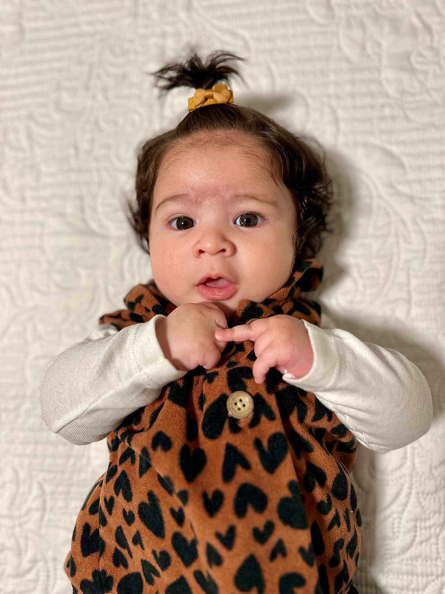 Chloe joined the competition — help win amazing prizes! baby, infant, child, face, eyes, hair, ponytail, expression, clothing, pattern, heart_pattern, button, blanket, texture, portrait, cute, lying_down, hands, white_sleeves, indoor