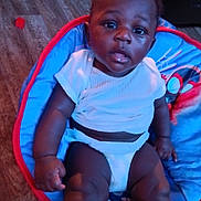 Keyshawn Jefferson is registered to the contest to win money with this photo: baby, child, infant, diaper, white_shirt, blue_chair, red_border, wooden_floor, indoors, seated, person, cute, young_child, looking_up, plush_chair, home, comfort, skin, expression, furniture