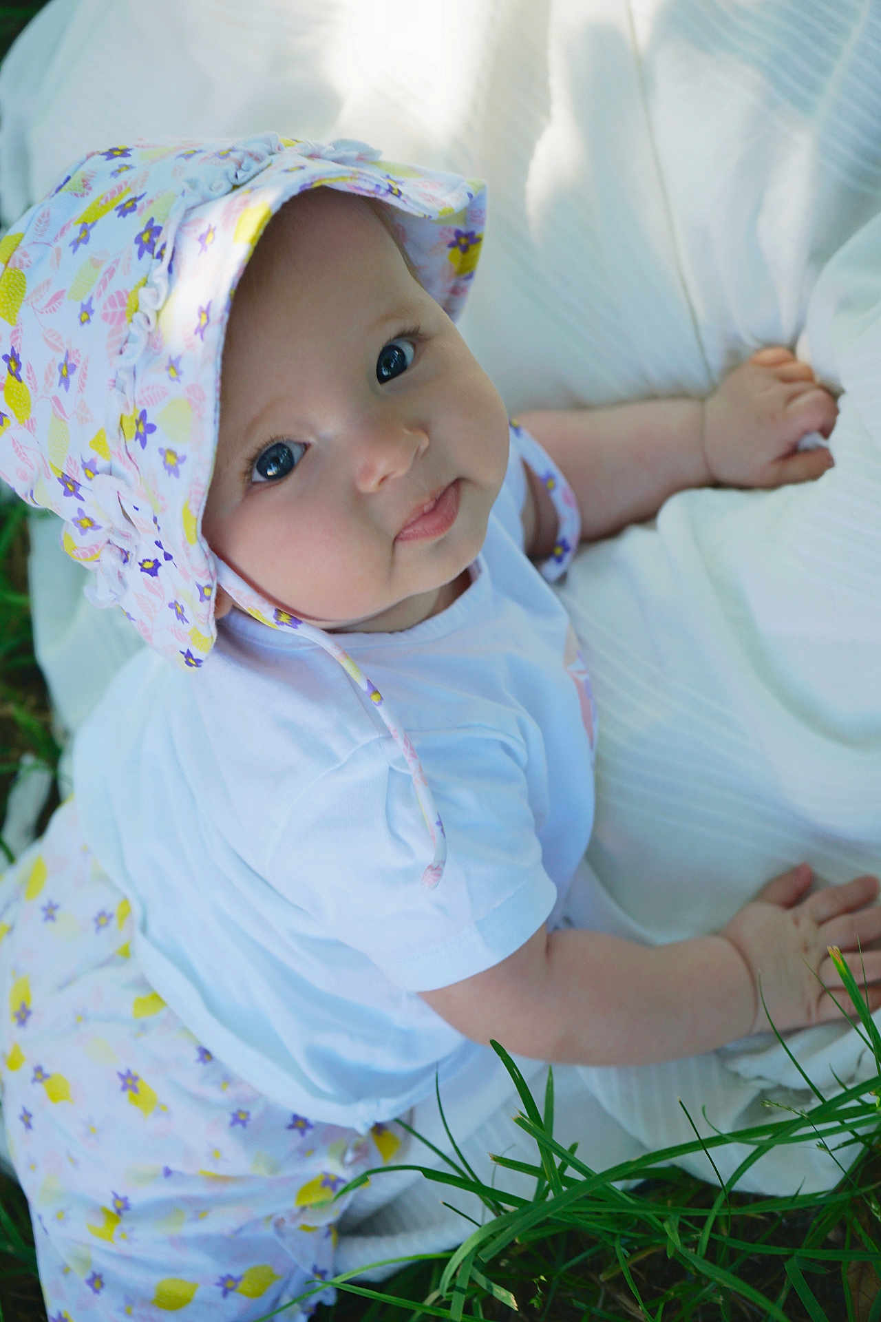 Hisaé a rejoint le concours — aidez-le/la à gagner de superbes lots ! baby, infant, child, hat, floral, white_clothing, blanket, grass, outdoor, cute, smile, face, eyes, skin, hand, nature, lying, person, young, sunlight