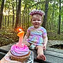 toddler, birthday, cupcake, candle, number_one, headband, forest, outdoor, bench, smile, child, dress, diaper, nature, celebration, person, happy, wood, sunlight, hand