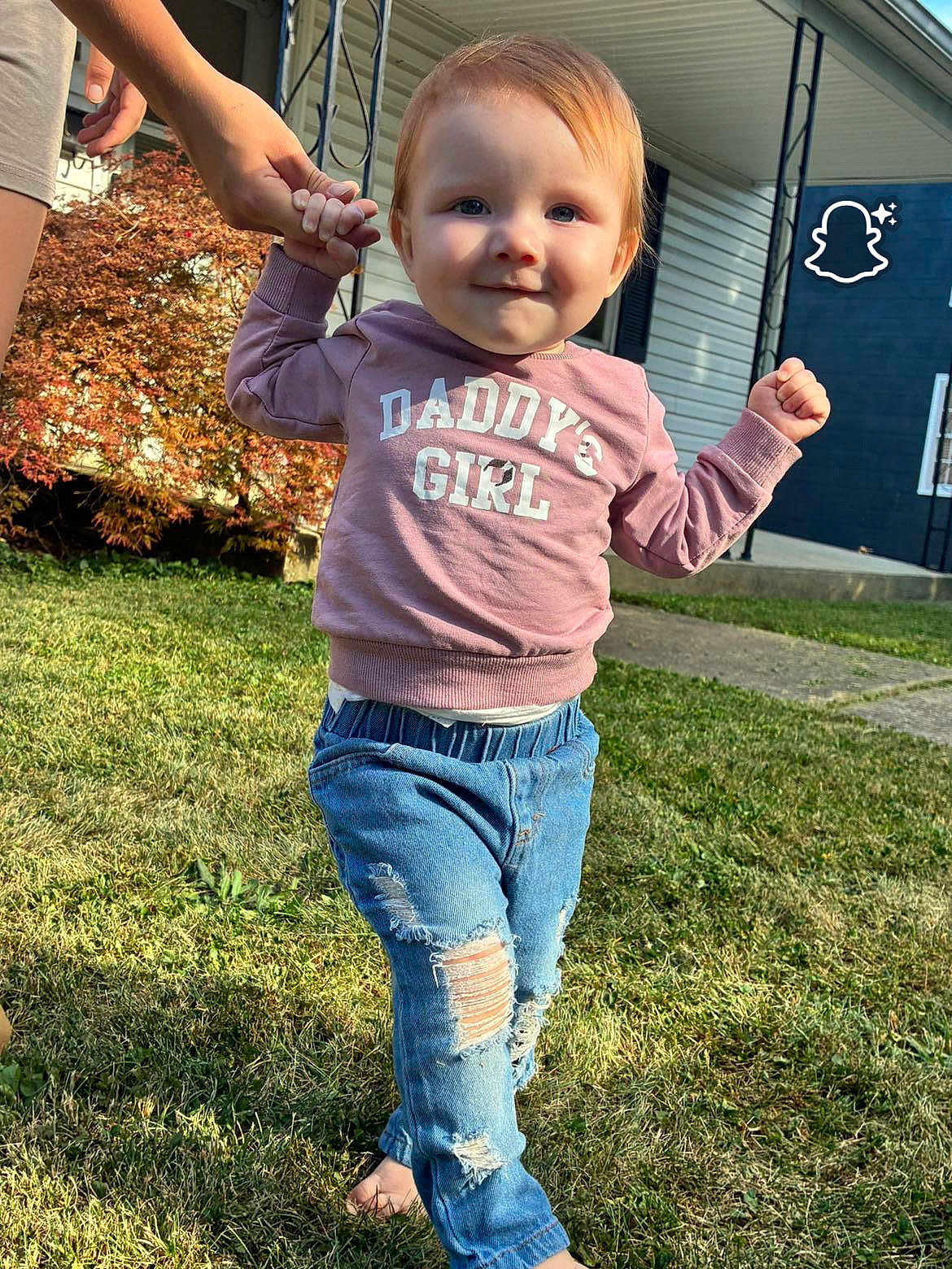 Azelia Lynn is registered to the contest to win money with this photo: toddler, child, walking, holding_hand, pink_sweatshirt, ripped_jeans, barefoot, grass, outdoor, house, autumn, bushes, sunlight, person, casual_clothing, smiling, blue_eyes, young_child, family, support