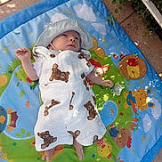Naël participe au concours pour gagner de l'argent avec cette photo : baby, infant, hat, overalls, bear_print, play_mat, outdoor, sunlight, shade, cartoon_animals, grass, leaves, colorful, child, cute, baby_clothes, relaxing, small, person, nature