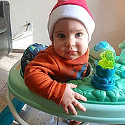 Yadira is registered to the contest to win money with this photo: toddler, baby, child, hat, red_hat, face, eyes, baby_walker, toy, hand, floor, tile_floor, indoor, clothing, long_sleeve, orange_sweater, home, furniture, cute, portrait