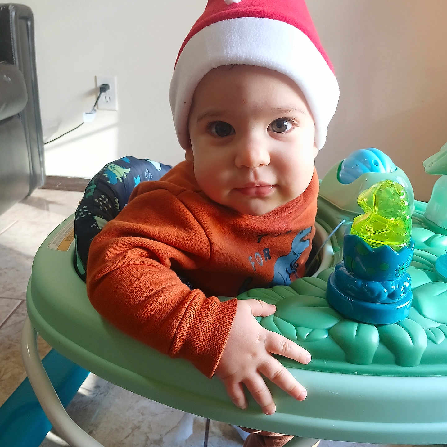 Yadira is registered to the contest to win money with this photo: baby, baby_walker, child, clothing, cute, eyes, face, floor, furniture, hand, hat, home, indoor, long_sleeve, orange_sweater, portrait, red_hat, tile_floor, toddler, toy