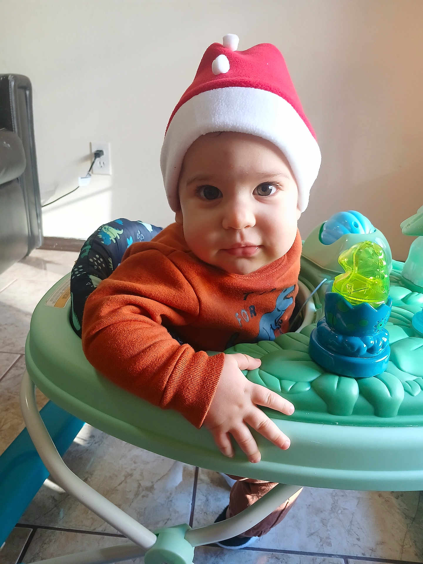 Yadira is registered to the contest to win money with this photo: toddler, baby, child, hat, red_hat, face, eyes, baby_walker, toy, hand, floor, tile_floor, indoor, clothing, long_sleeve, orange_sweater, home, furniture, cute, portrait