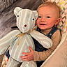 baby, child, teddy_bear, toy, smile, happy, face, blue_eyes, denim_overalls, sweater, cushion, chair, indoor, plush, patterned_fabric, person, infant, cute, cozy, comfort