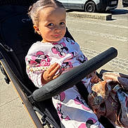 Zayna participe au concours pour gagner de l'argent avec cette photo : accessory, baby, child, clothing, cute, face, hand, minnie_mouse, outdoor, pacifier, person, playful, sidewalk, smile, stroller, sunlight, toddler, urban, van, vehicle