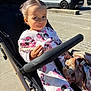 accessory, baby, child, clothing, cute, face, hand, minnie_mouse, outdoor, pacifier, person, playful, sidewalk, smile, stroller, sunlight, toddler, urban, van, vehicle