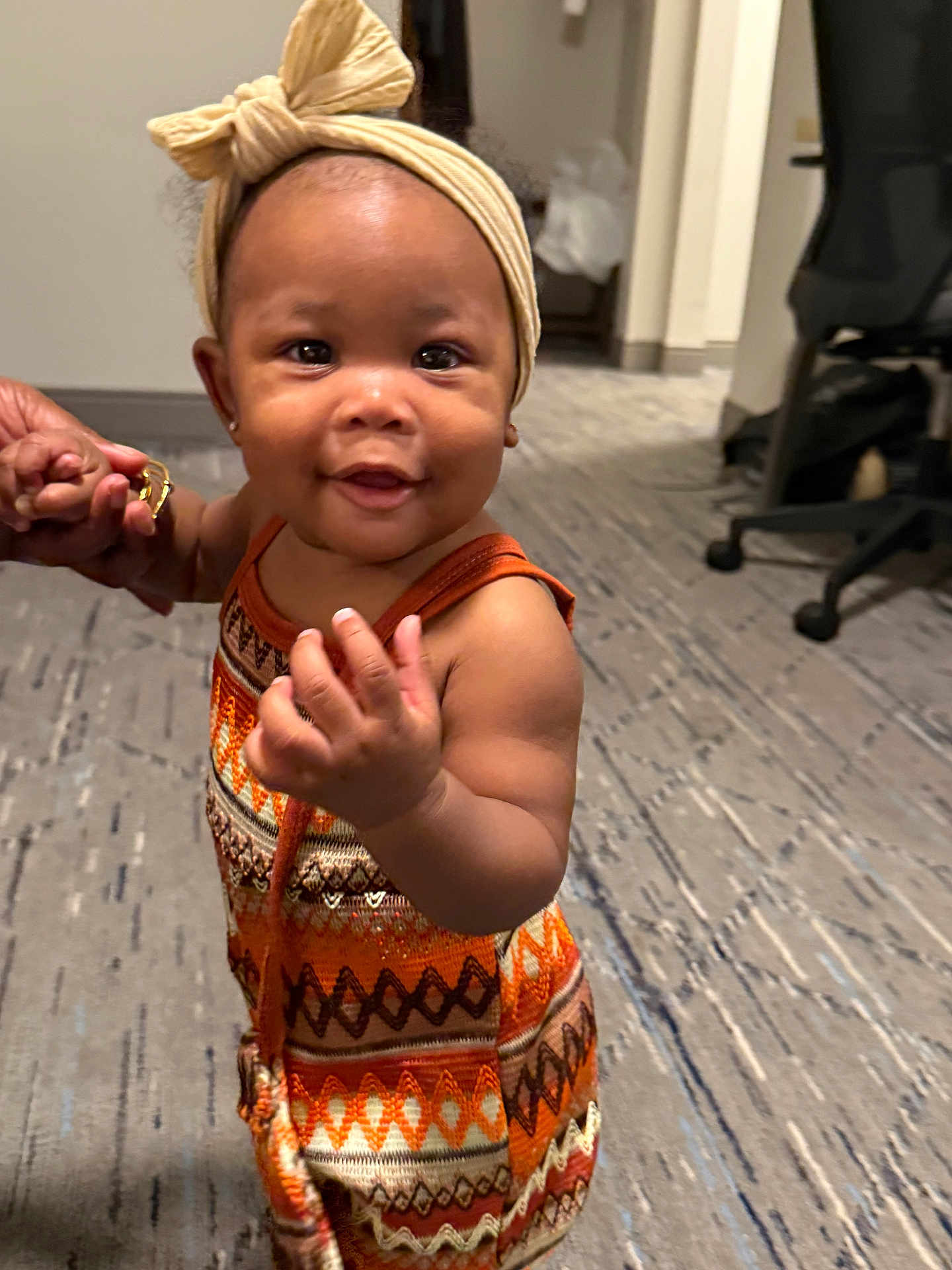 Aubrielle joined the competition — help win amazing prizes! toddler, child, smiling, headband, bow, colorful_clothing, hand_holding, carpet, indoor, office_chair, person, cute, baby, portrait, standing, happy, skin, face, young_child, support