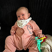 Levi joined the competition — help win amazing prizes! baby, infant, smile, onesie, bib, toy, plastic_rings, couch, fabric, striped_clothing, hand, footed_pajamas, comfort, cute, child, indoor, happy, portrait, seated, play