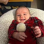 baby, smiling, infant, red_clothing, plaid, pom_pom, cushion, hand, face, indoor, furniture, table, baby_monitor, foot, patterned_fabric, happy, cozy, person, portrait, child