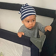 Adriel participe au concours pour gagner de l'argent avec cette photo : baby, child, curious, expression, face, gray_clothing, grip, hands, home, indoor, mesh_sides, person, plastic, playpen, standing, striped_beanie, toddler, toy, young, young_child